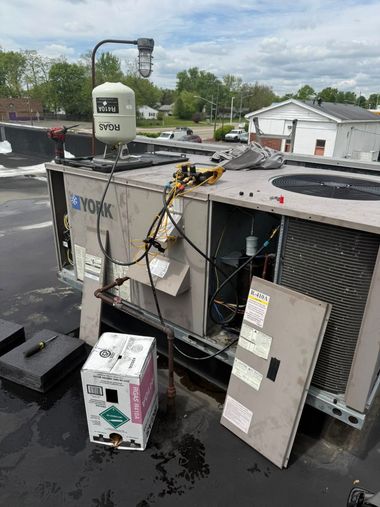 Damaged rooftop HVAC unit with open panels and water pooling on a wet parking lot.