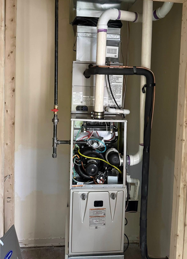 Open furnace and water heater in a narrow utility closet with exposed pipes and wiring