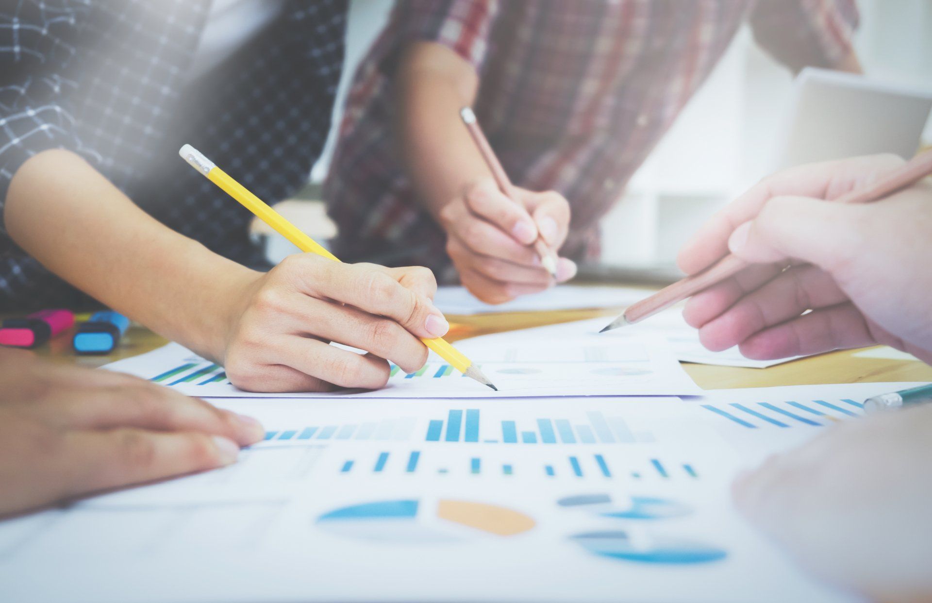 People collaborating, pointing at business charts and graphs on a table with pencils.