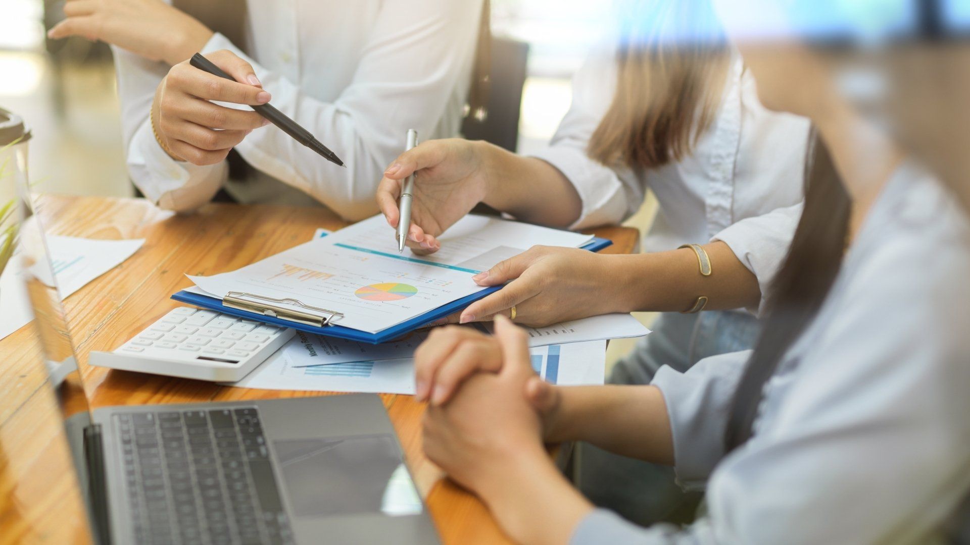 Three people reviewing charts and data during a meeting at a table, using pens and a laptop.