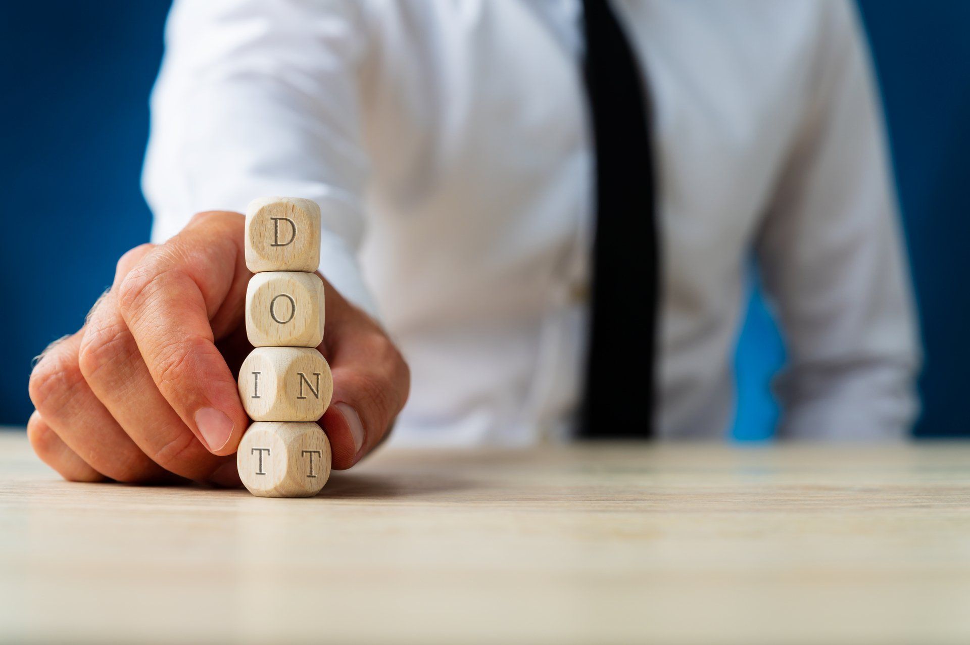 A person in a white shirt and tie stacks wooden blocks spelling