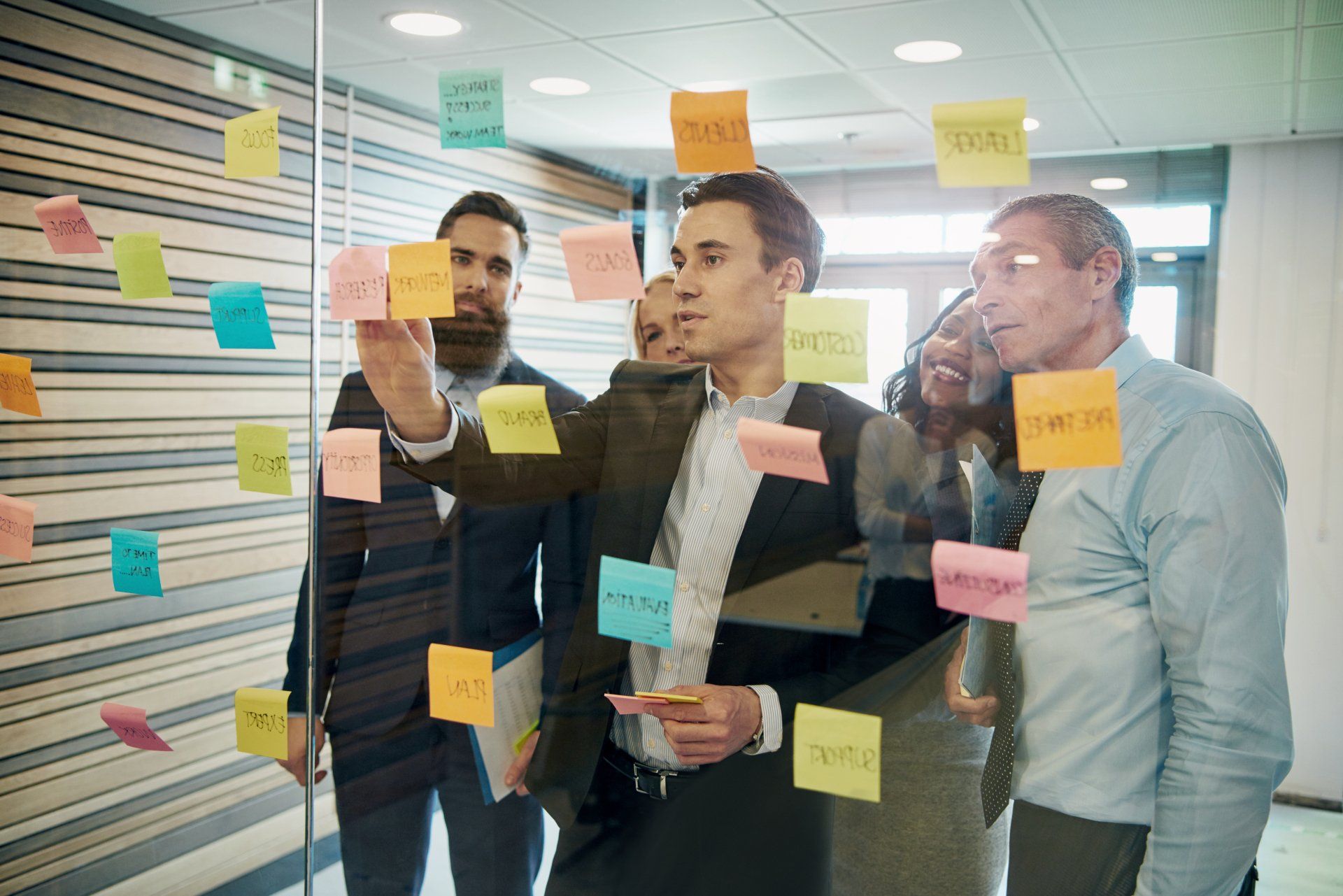 Business team brainstorming, using sticky notes on a glass wall.