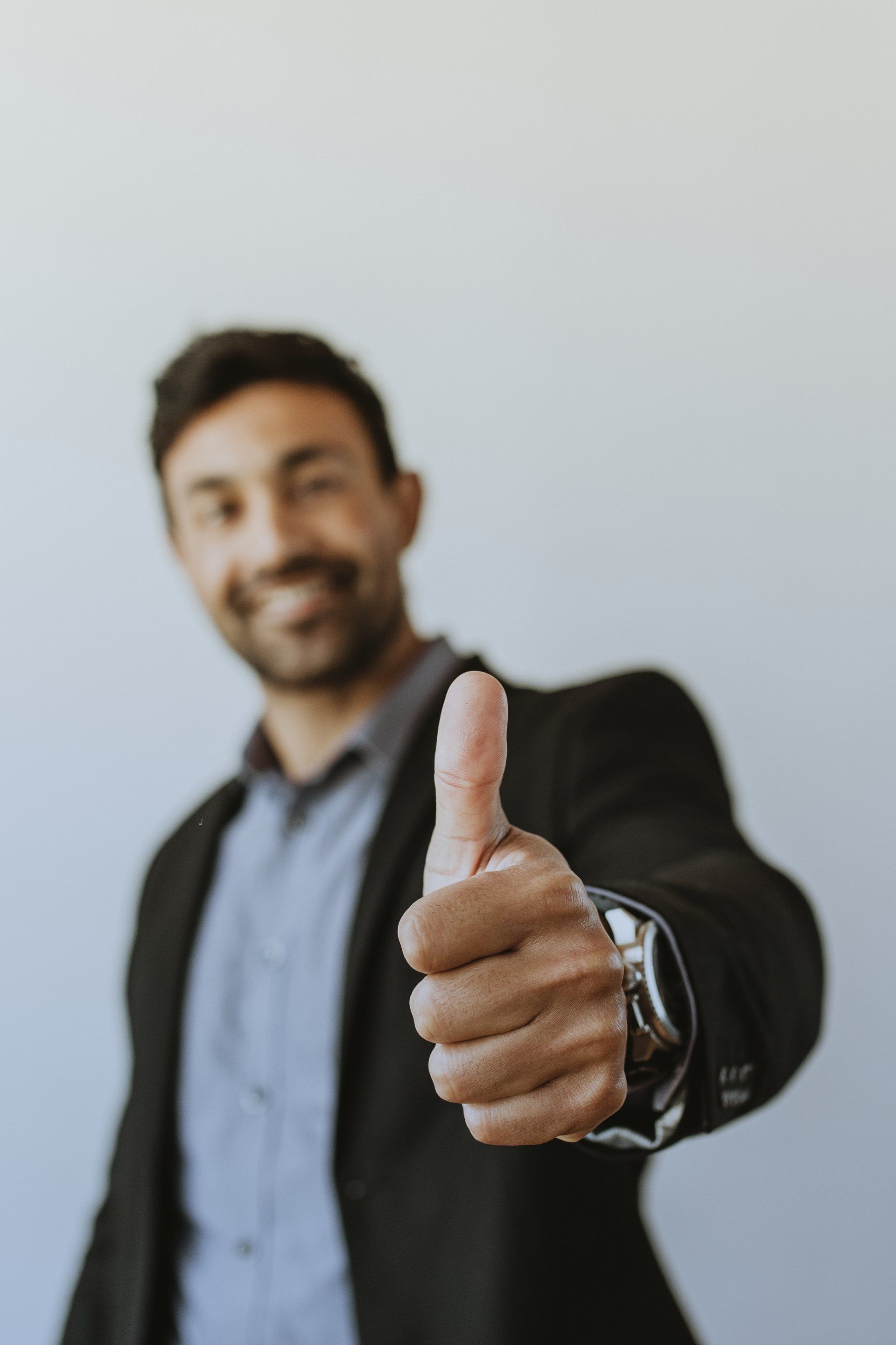 Man in blazer giving thumbs up, smiling.