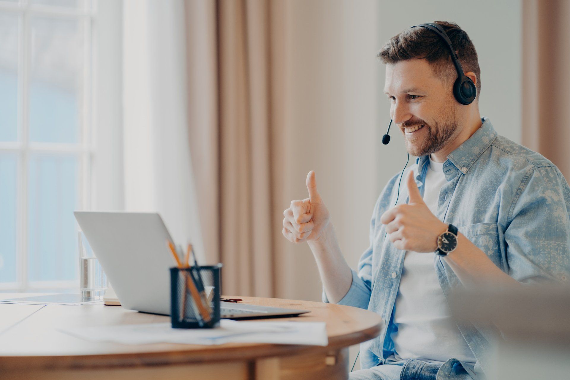Man with headset gives two thumbs up during a video call on his laptop.