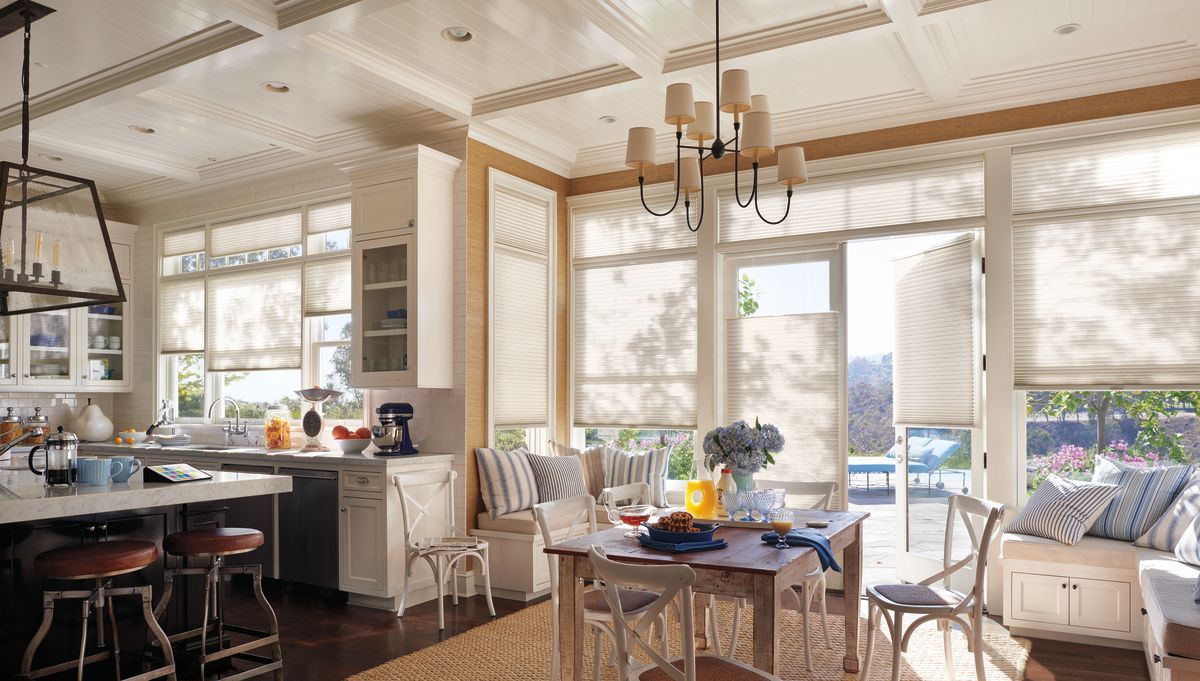A bright, airy kitchen and dining area with white cabinetry, a wooden table, farmhouse-style chairs, and large windows.