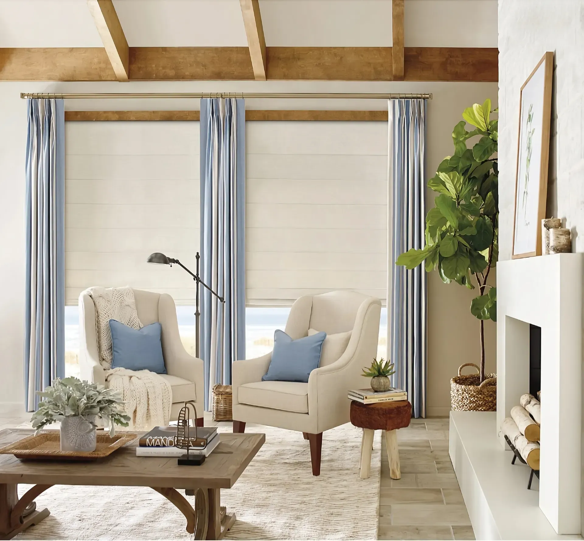 Two cream armchairs with blue pillows in a cozy living room with striped curtains, a wooden coffee table, and a fireplace.