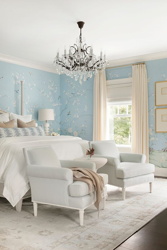 Soft blue bedroom with patterned wallpaper, fabric drapes, and Provenance® Woven Wood Shades.