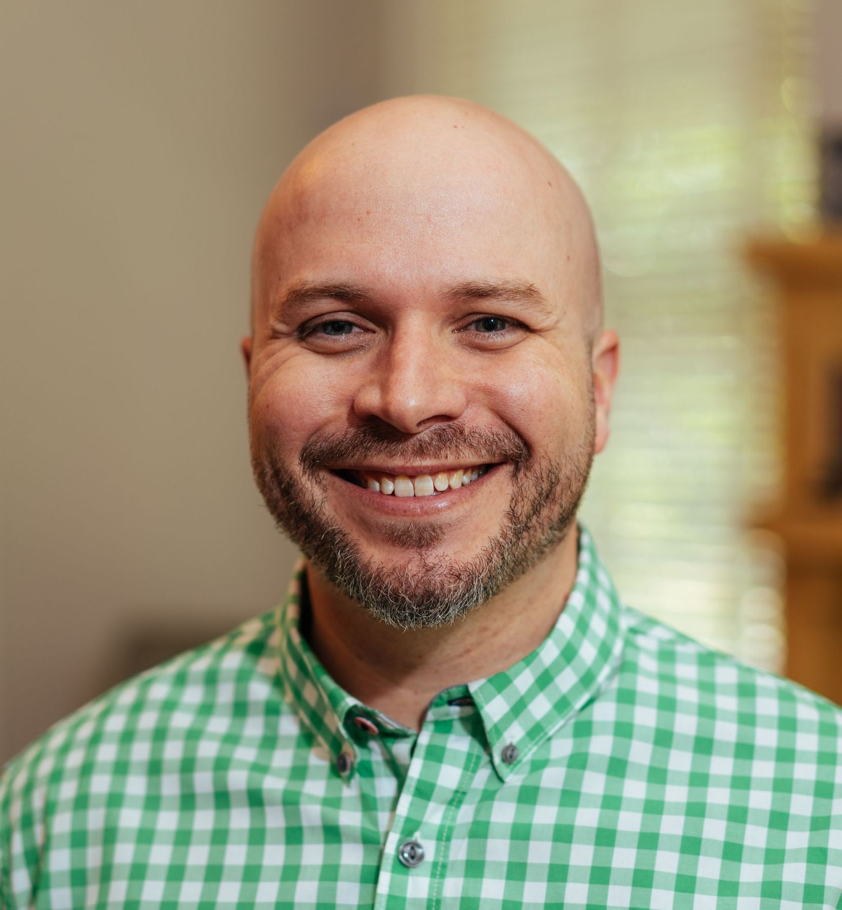 man wth a beard is wearing a green and white checkered shirt and smiling.