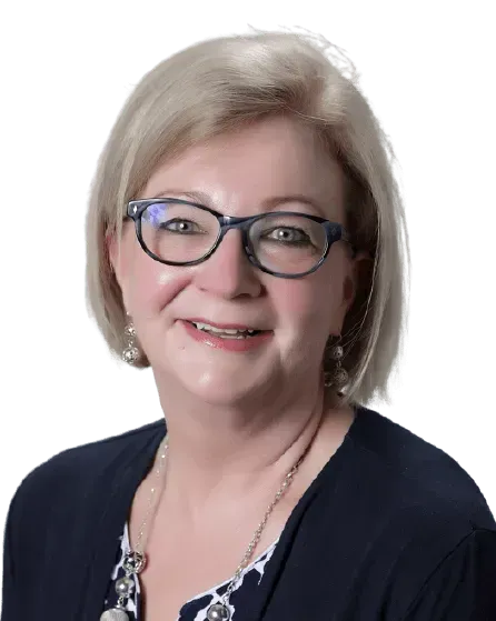 Headshot of a person with blonde hair, glasses, and a dark blue cardigan over a patterned top, smiling against white.
