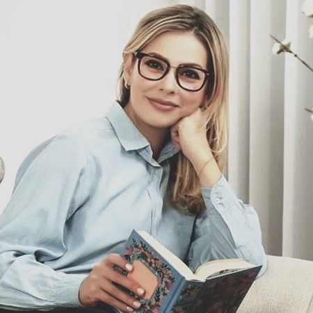 A woman wearing glasses is sitting on a couch reading a book.