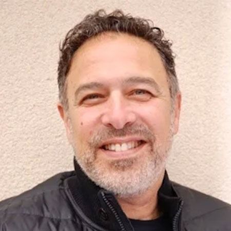 A man with a beard is smiling and wearing a black jacket.