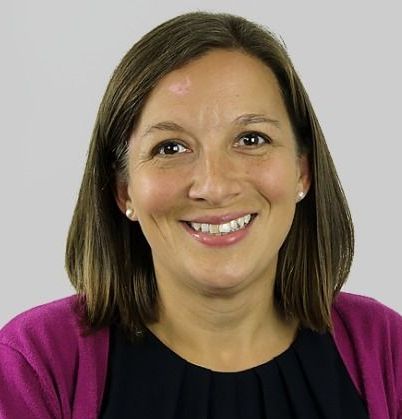 A woman wearing a pink cardigan and a black shirt is smiling.