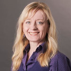 A woman with blonde hair is smiling for the camera while wearing a purple shirt.