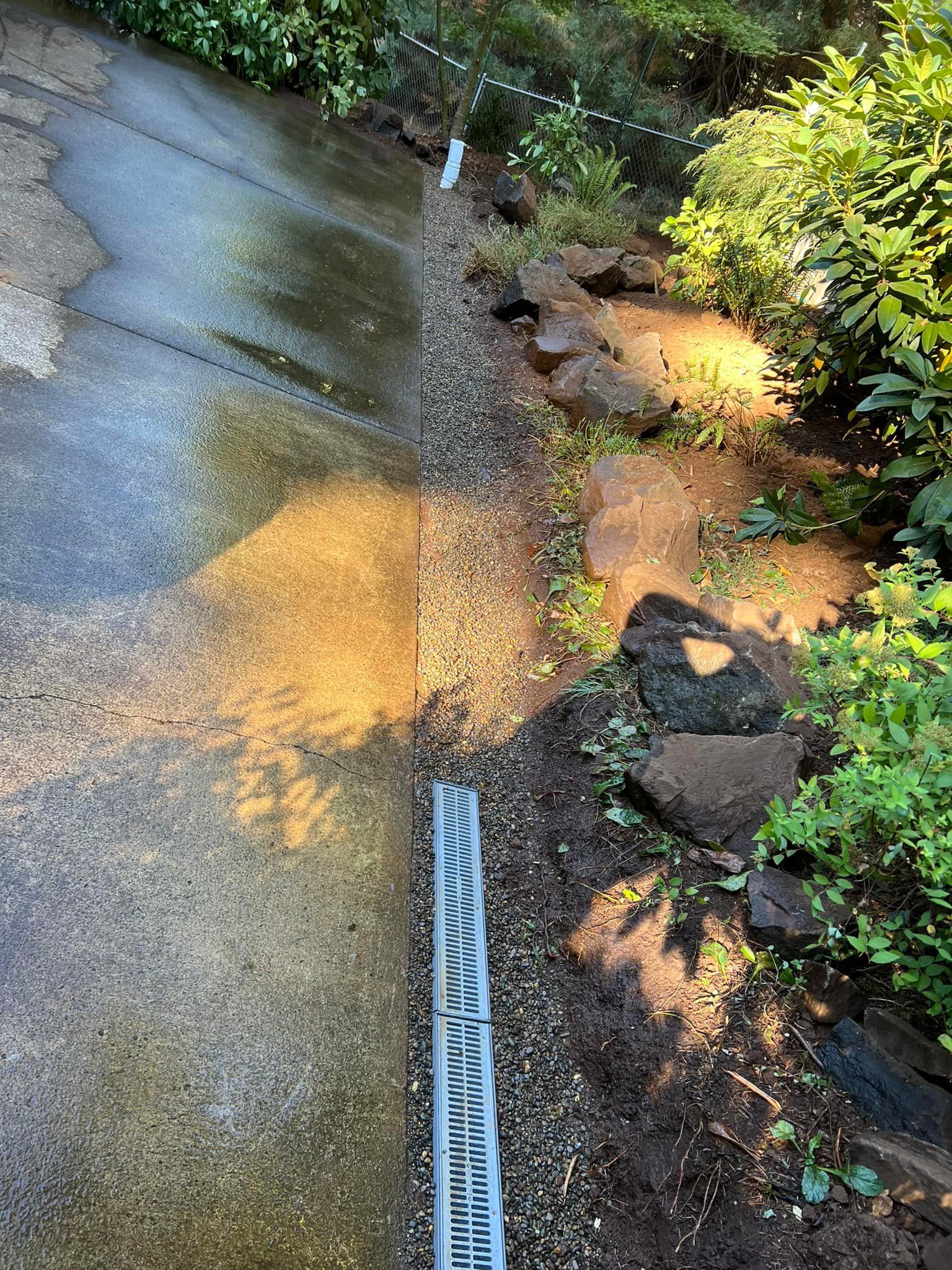 A drain on the side of a driveway next to a rock wall.
