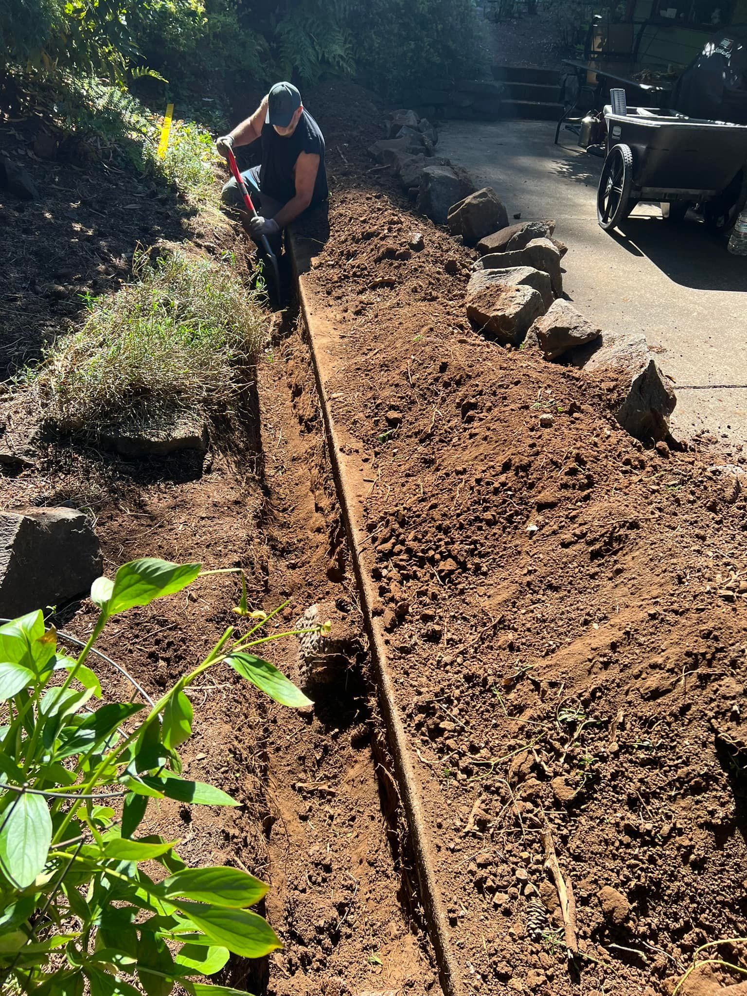 A man is kneeling down in the dirt with a shovel.