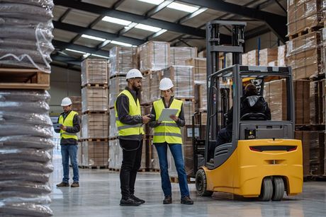 A group of workers are standing in a warehouse next to a forklift.
