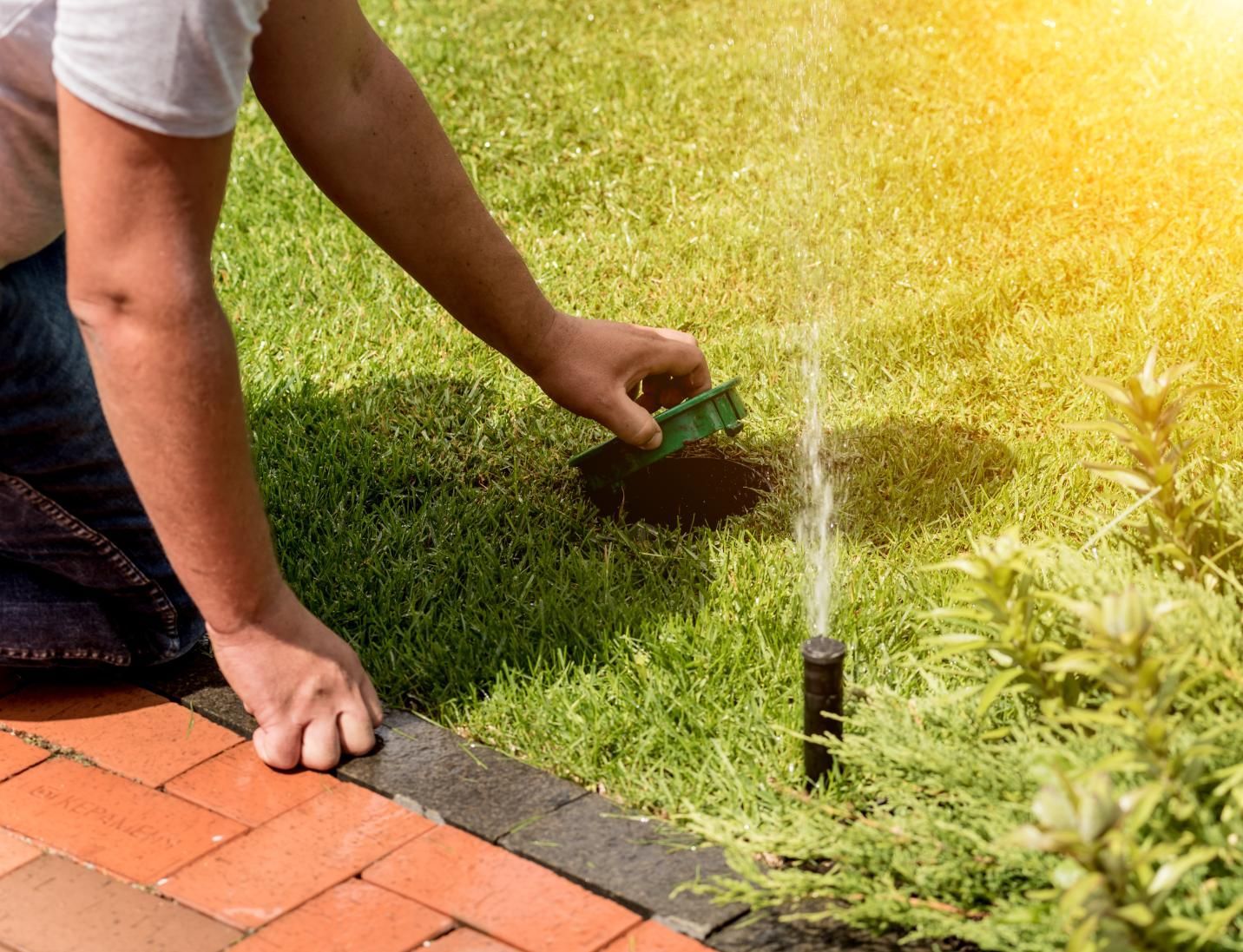 A man is kneeling down to fix a lawn sprinkler.