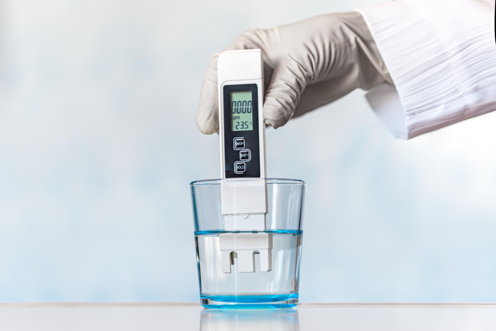 A person is holding a digital thermometer over a glass of water.