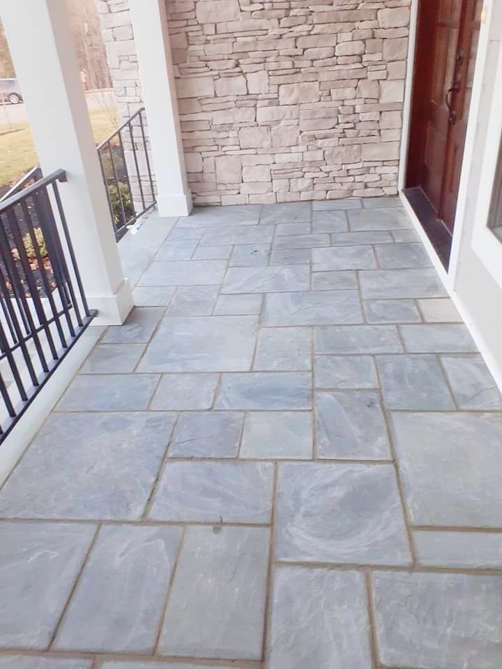 A porch with a stone wall and a gray tile floor