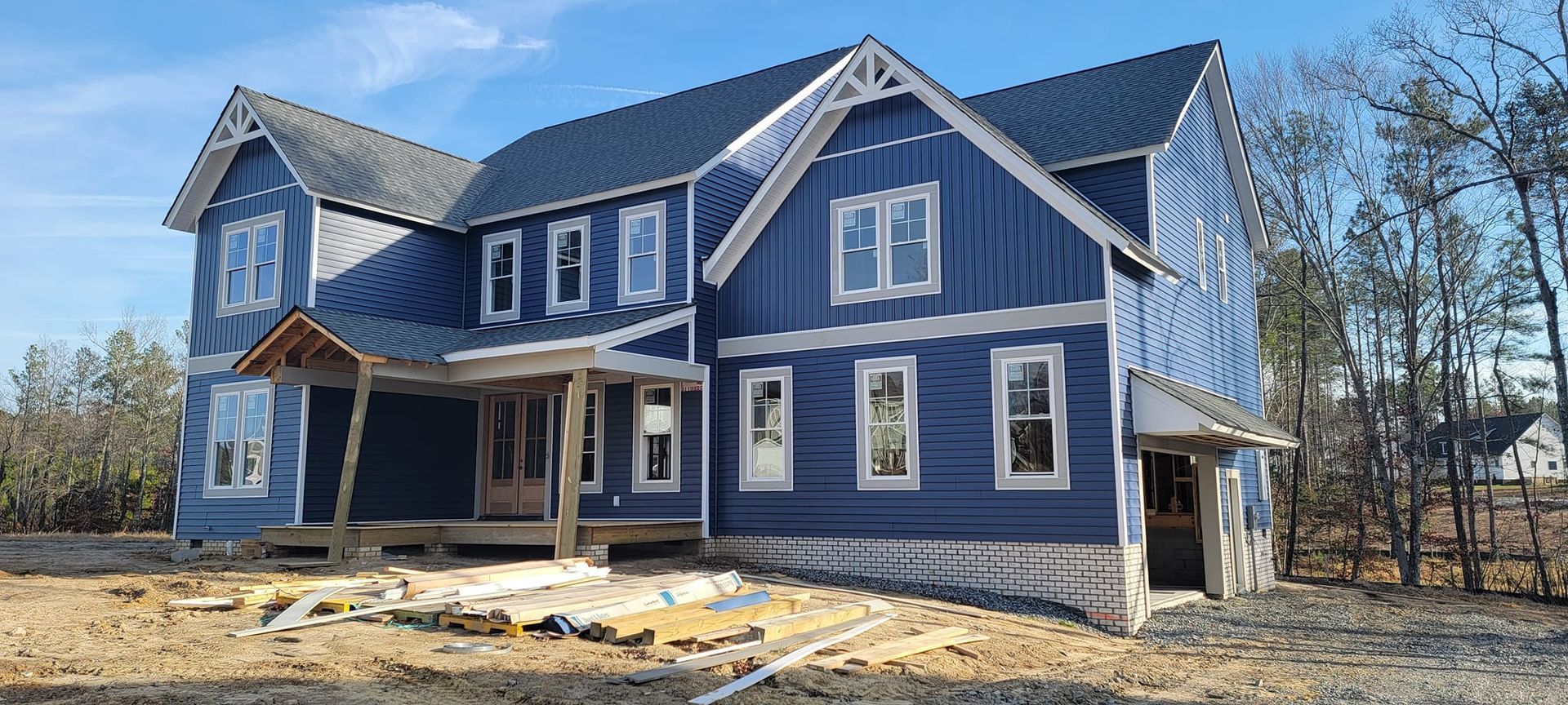 A large blue house is being built in the middle of a dirt field.
