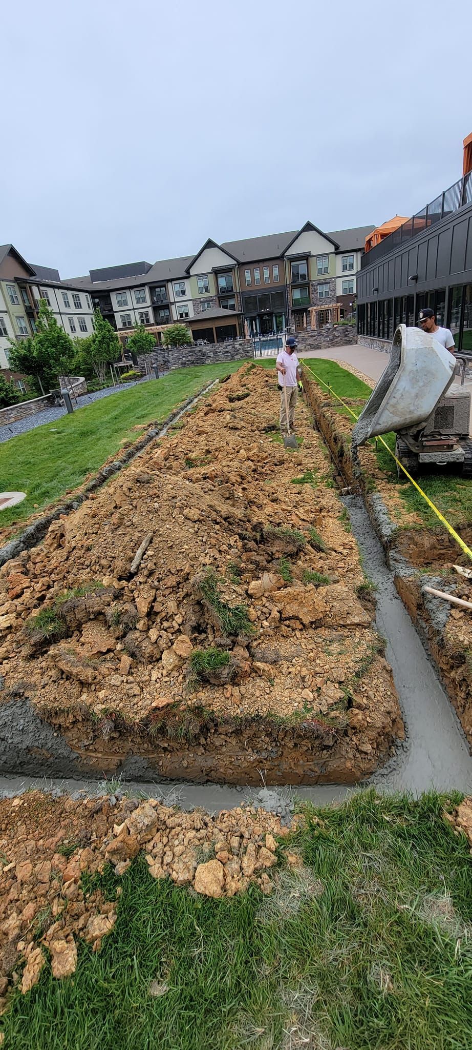 A concrete mixer is pouring concrete into a trench in a yard.