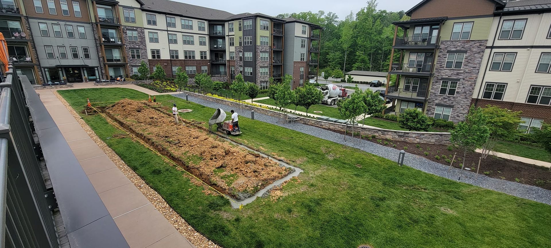 A lawn mower is cutting grass in front of a large apartment building.