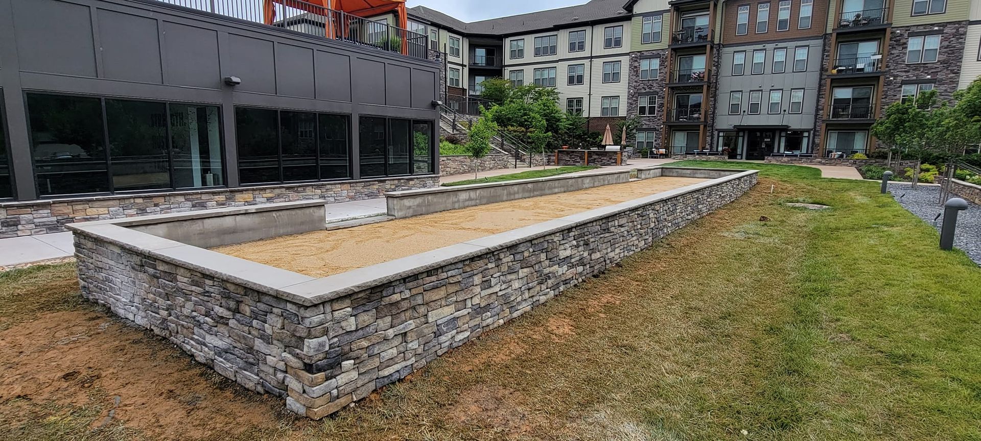 A large stone wall is sitting in the middle of a grassy field in front of a building.