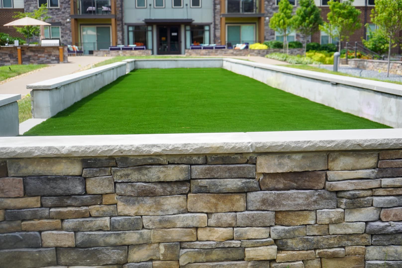 A stone wall surrounds a lush green field in front of a building.