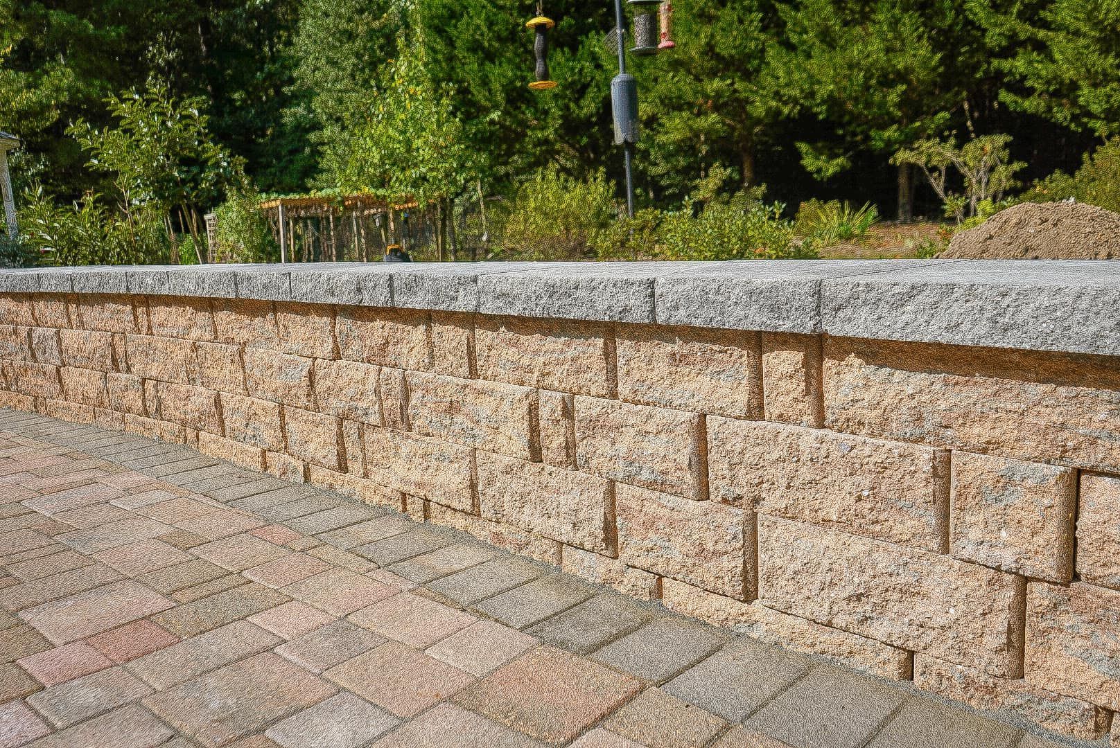 A brick wall along a brick walkway with trees in the background.
