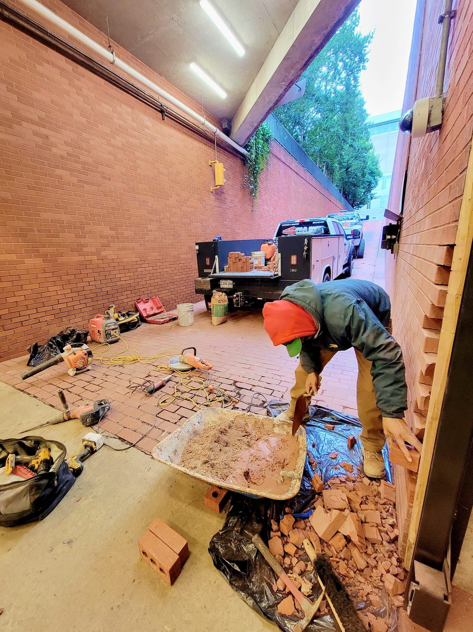 A man is working on a brick wall with a wheelbarrow full of bricks.
