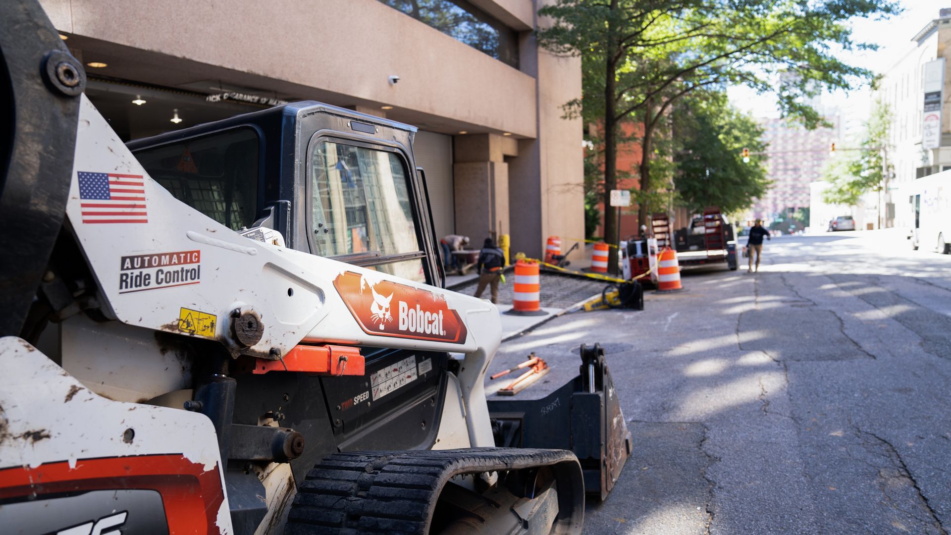 A bobcat tractor is parked on the side of a city street.