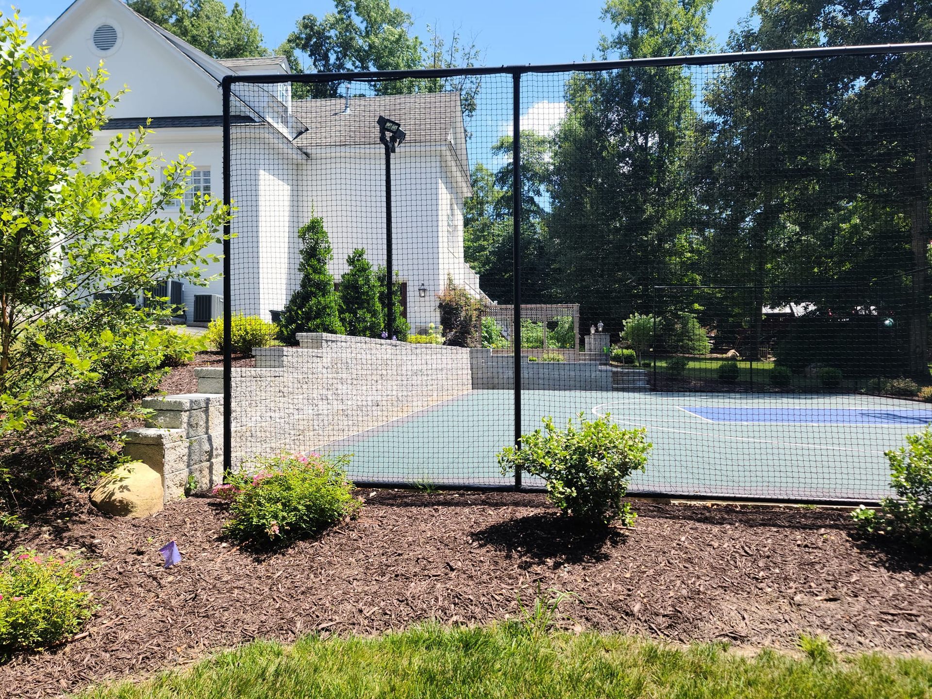 A tennis court is behind a fence in a backyard.