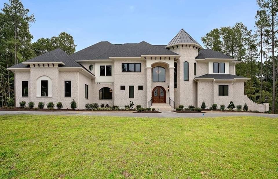 A Large White House With a Black Roof is Sitting on Top of a Lush Green Field