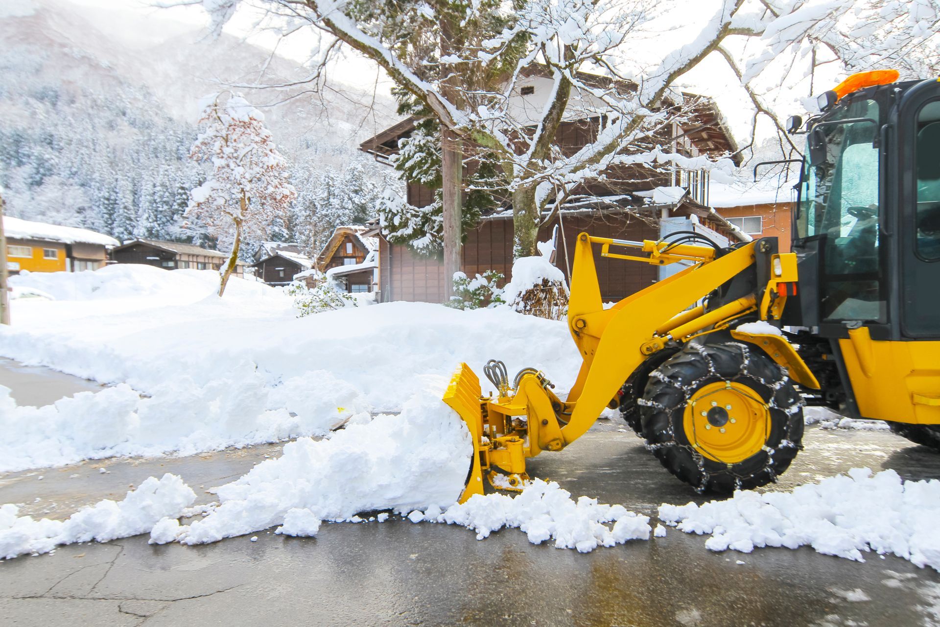 A Yellow Snow Plow is Clearing Snow From a Driveway