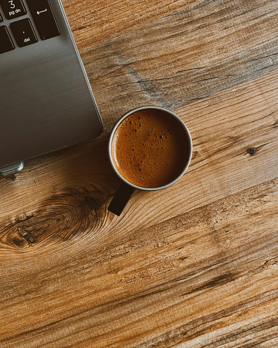 Top view of a coffee mug beside a laptop on a wooden desk