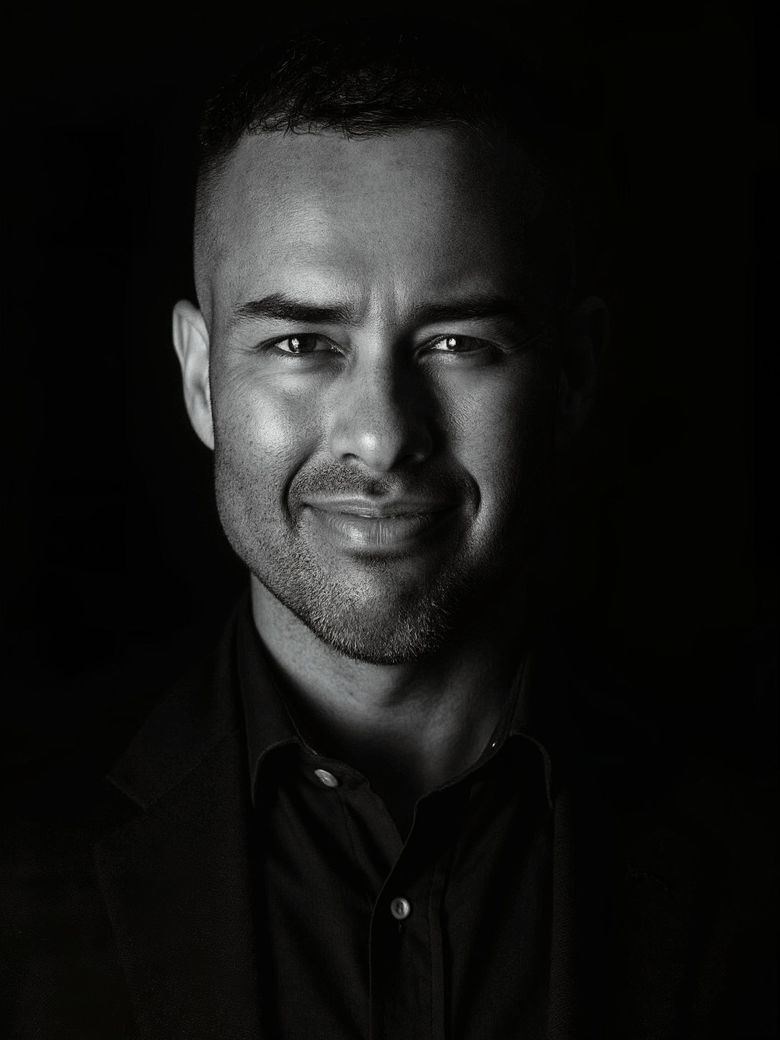 Portrait of a smiling man in dark clothing against a black background