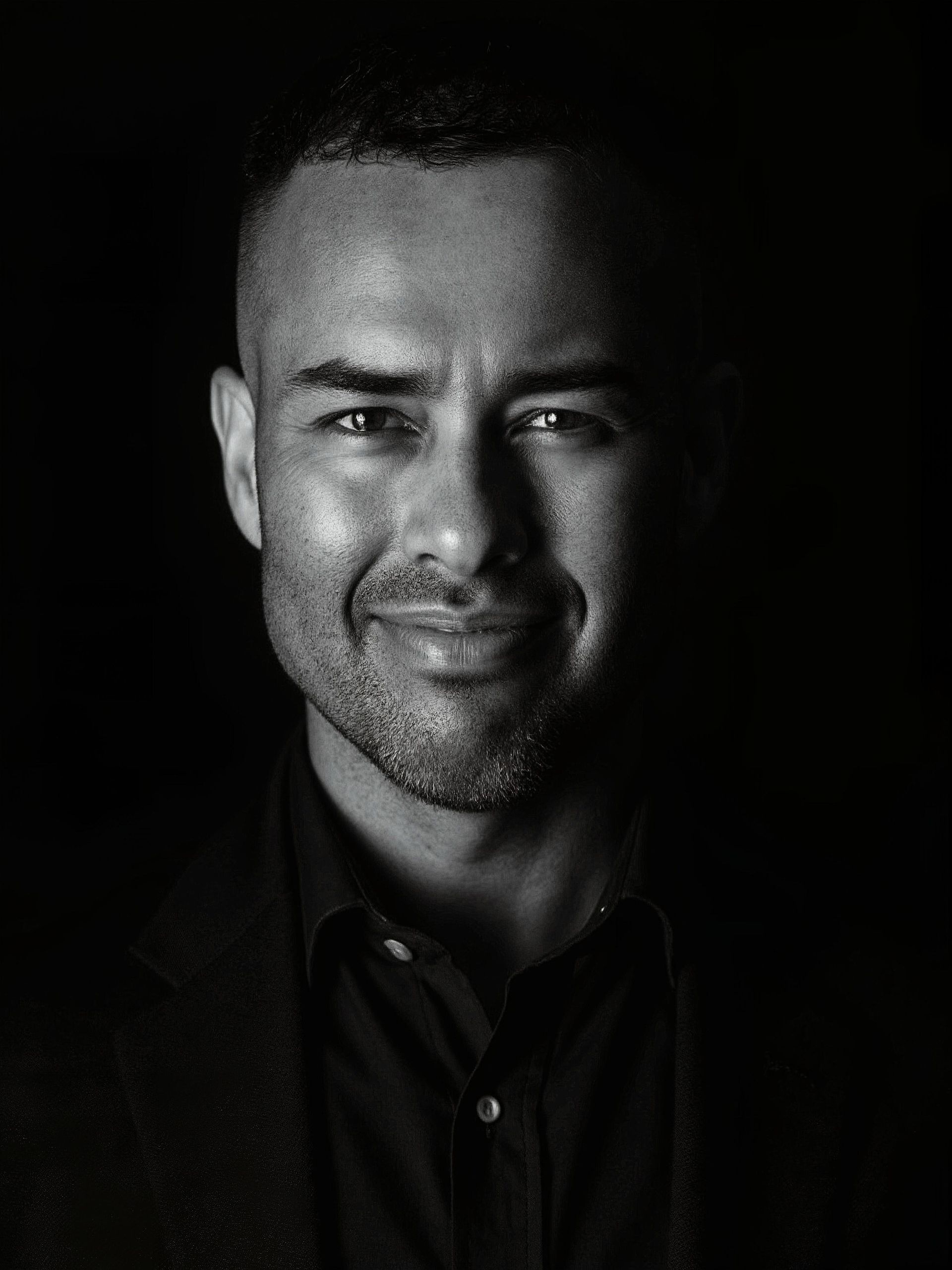 Portrait of a smiling man in dark clothing against a black background