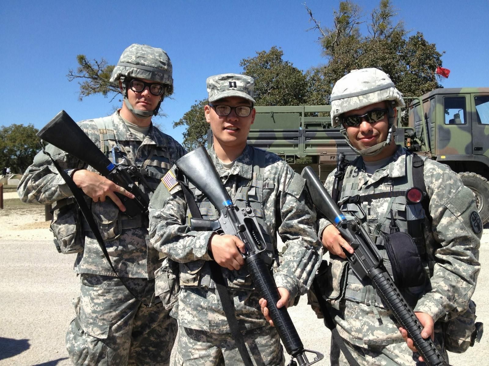 Three soldiers in camouflage uniforms holding rifles outdoors under a clear blue sky