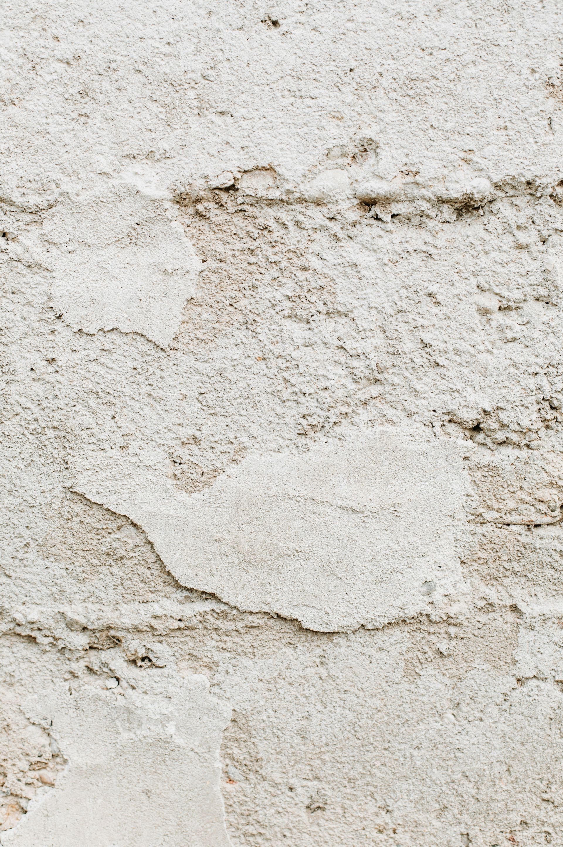 Close-up of a weathered white stucco wall with cracks and rough texture