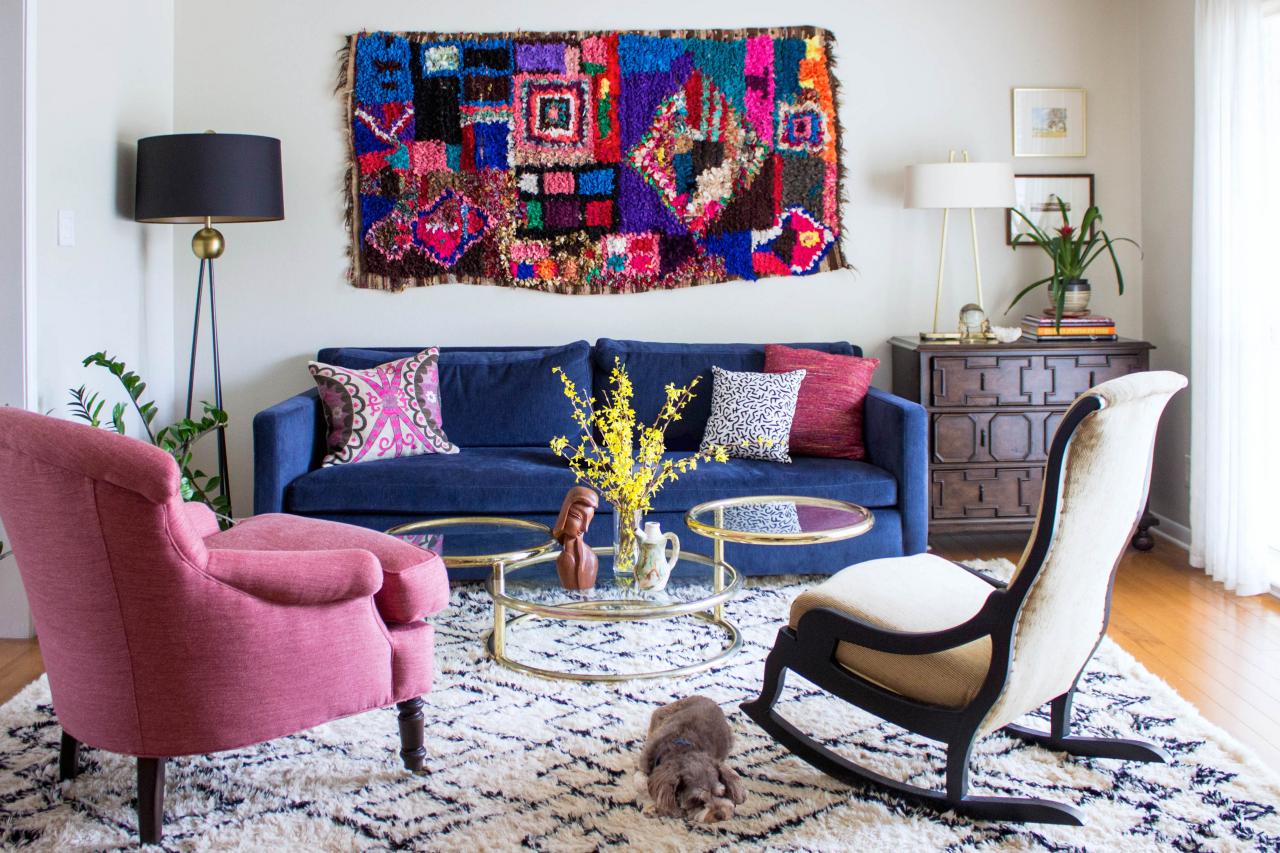 A living room with a blue couch , pink chairs , and a rocking chair.