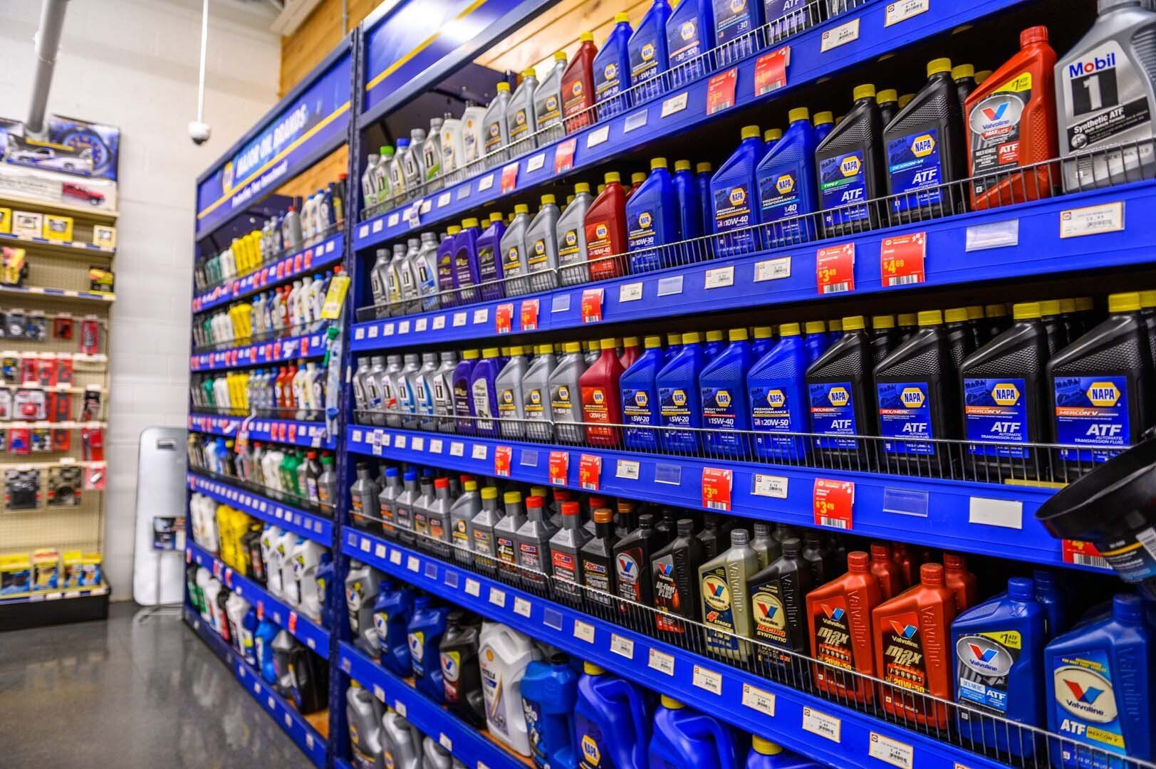 A retail aisle with blue shelving units stocked with rows of various motor oil bottles in a brightly lit store.