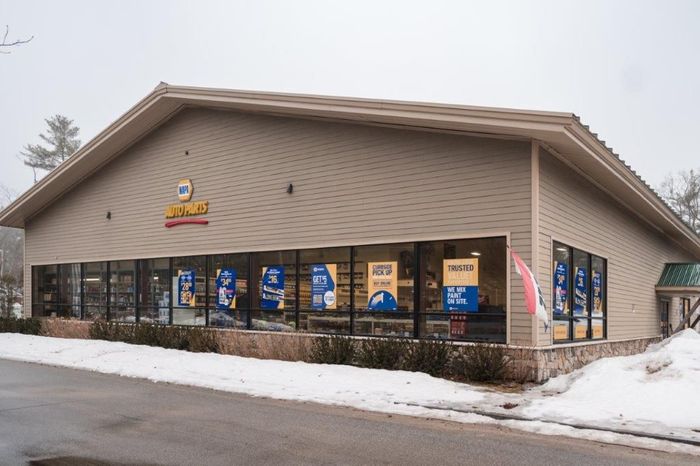 A NAPA Auto Parts store building with beige siding, large front windows, and a snow-covered parking area.