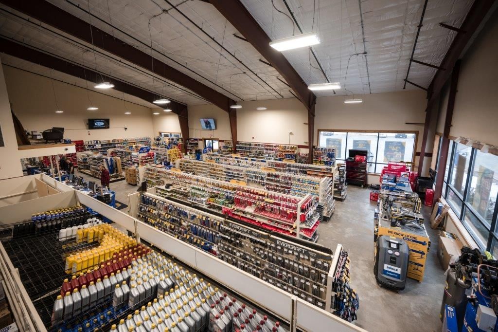 A wide-angle, high-angle view of a well-stocked retail hardware or automotive supply store with aisles of goods.