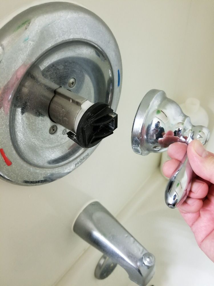 Hand removing a chrome shower handle, exposing the valve stem and wall plate