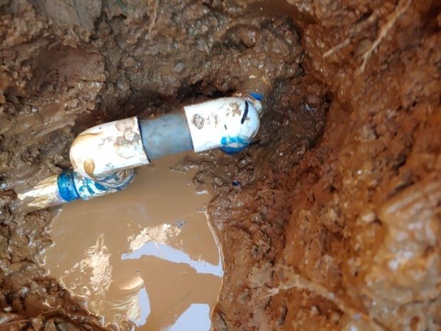 Buried pipe with blue-and-white fittings in muddy excavation trench, with standing water