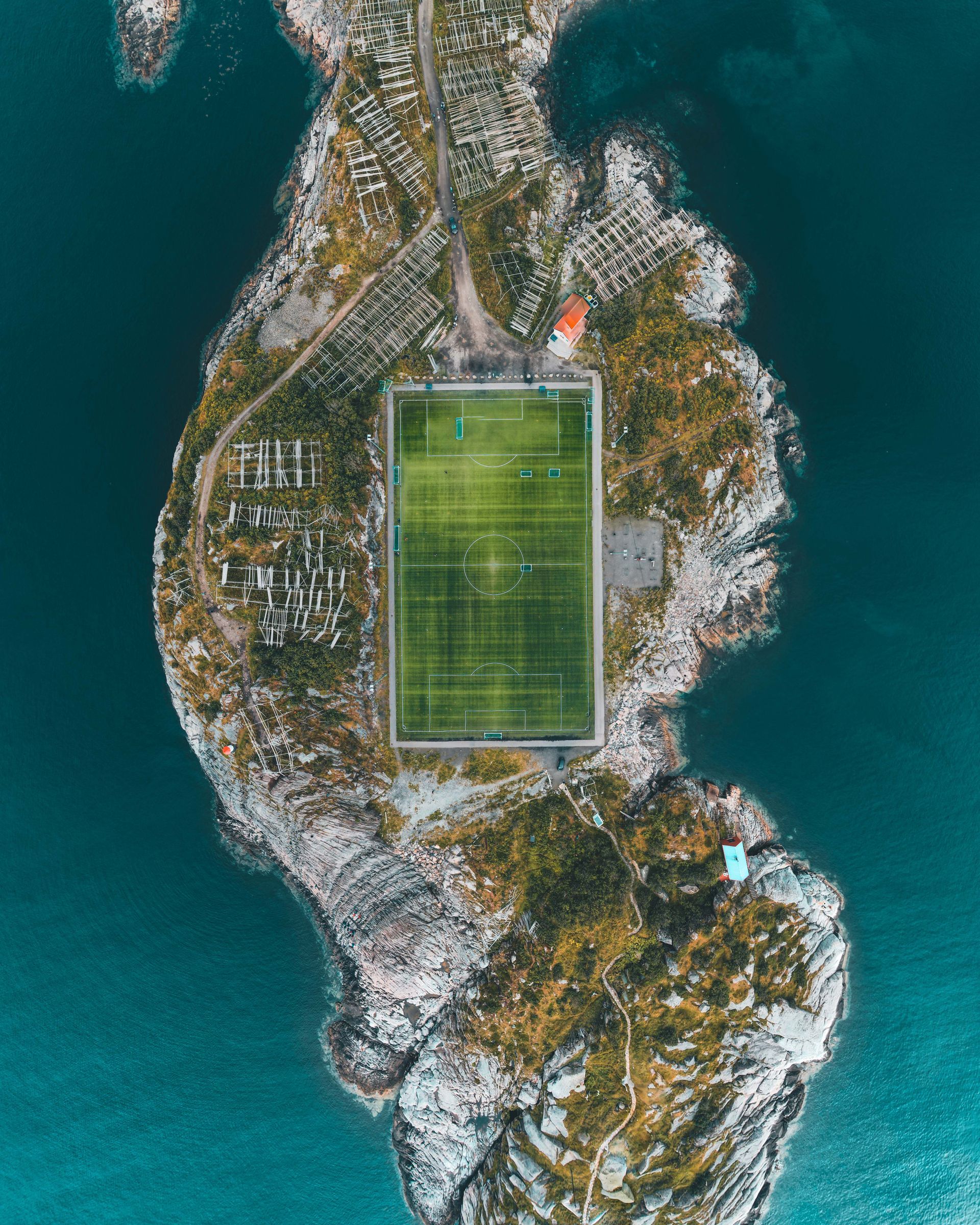 Luftfoto av en fotballbane på en liten, steinete øy omgitt av dypblått vann.