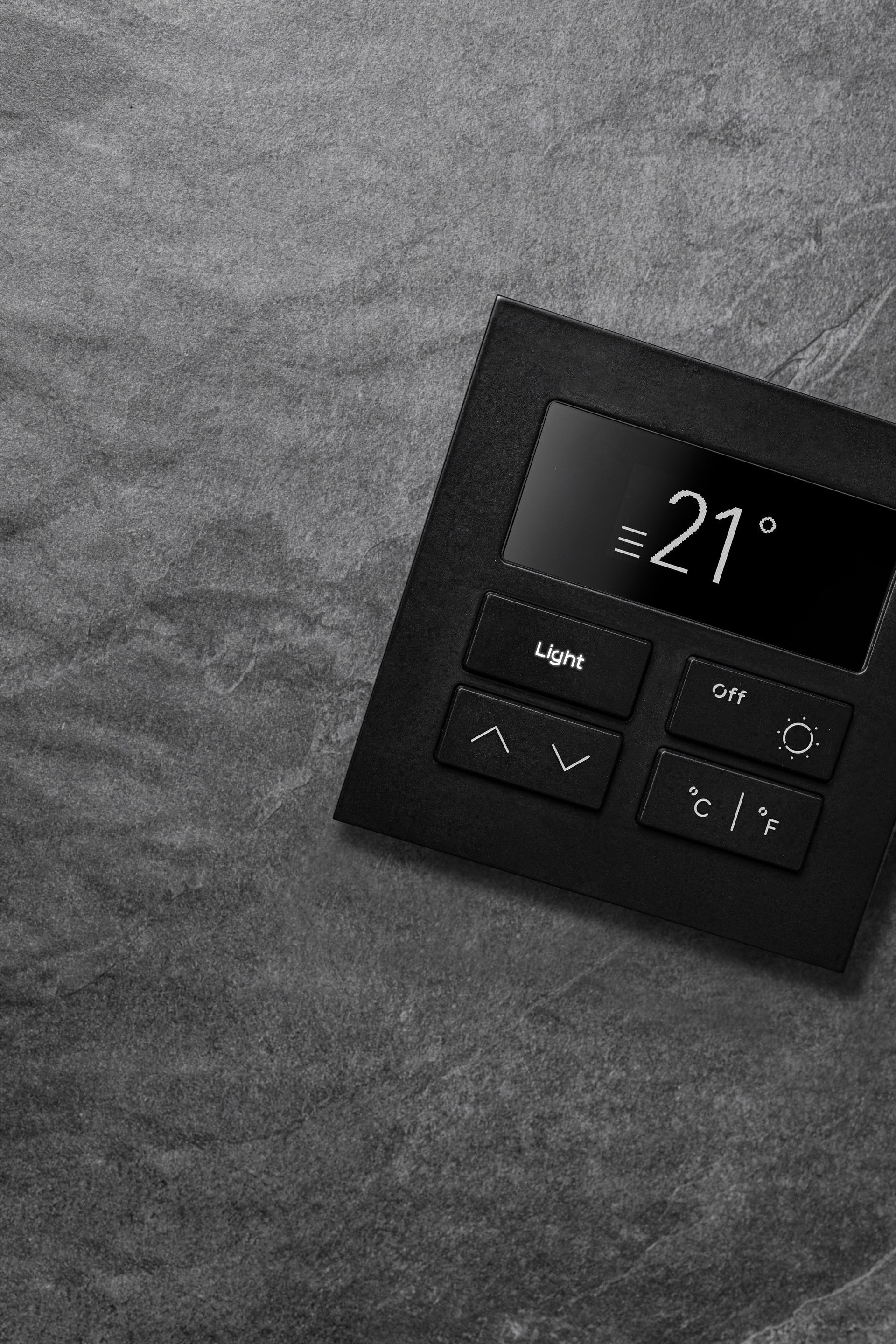 A black thermostat is sitting on a gray surface.