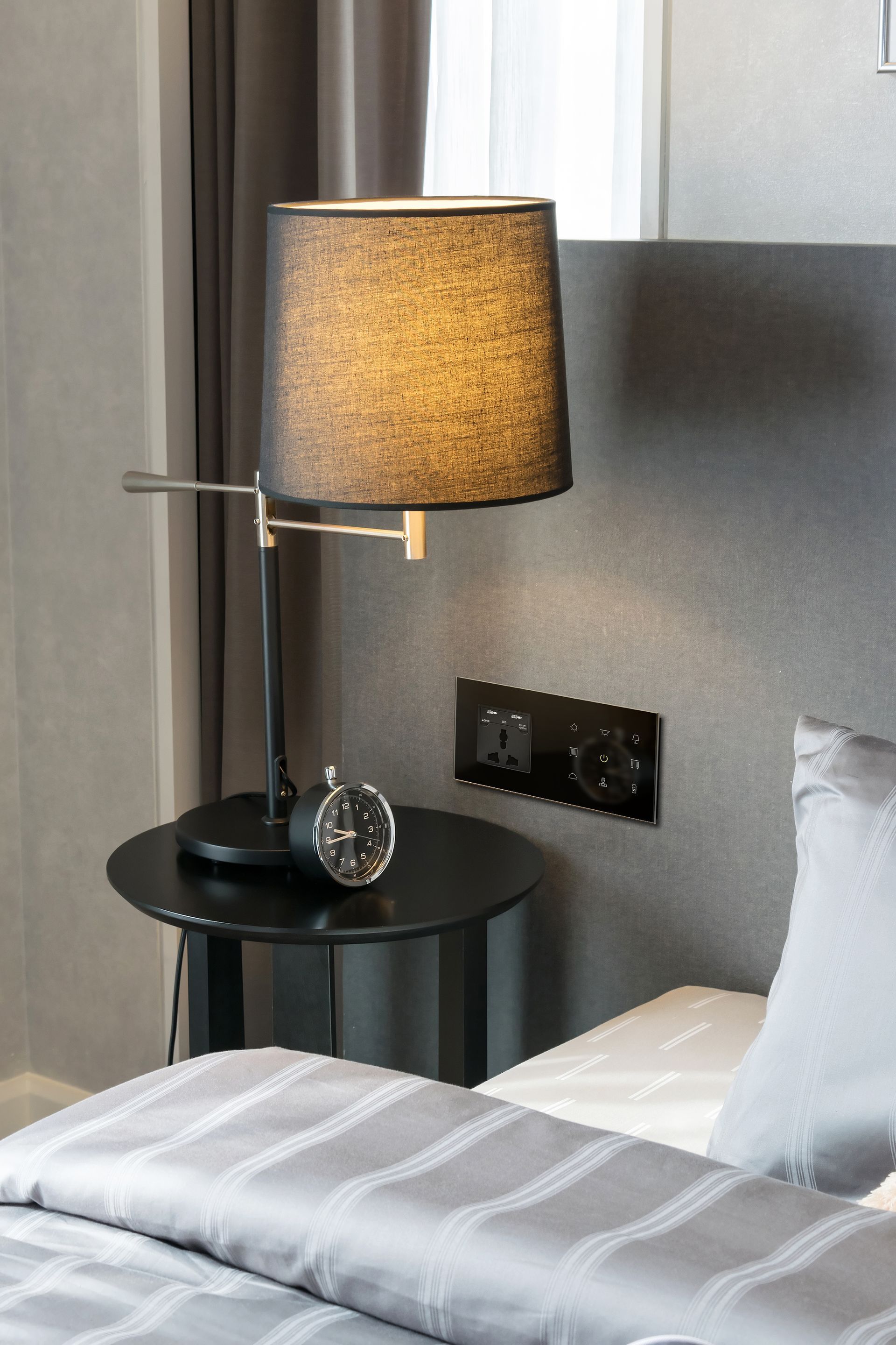 A bedroom with a bed , nightstand , lamp and clock.
