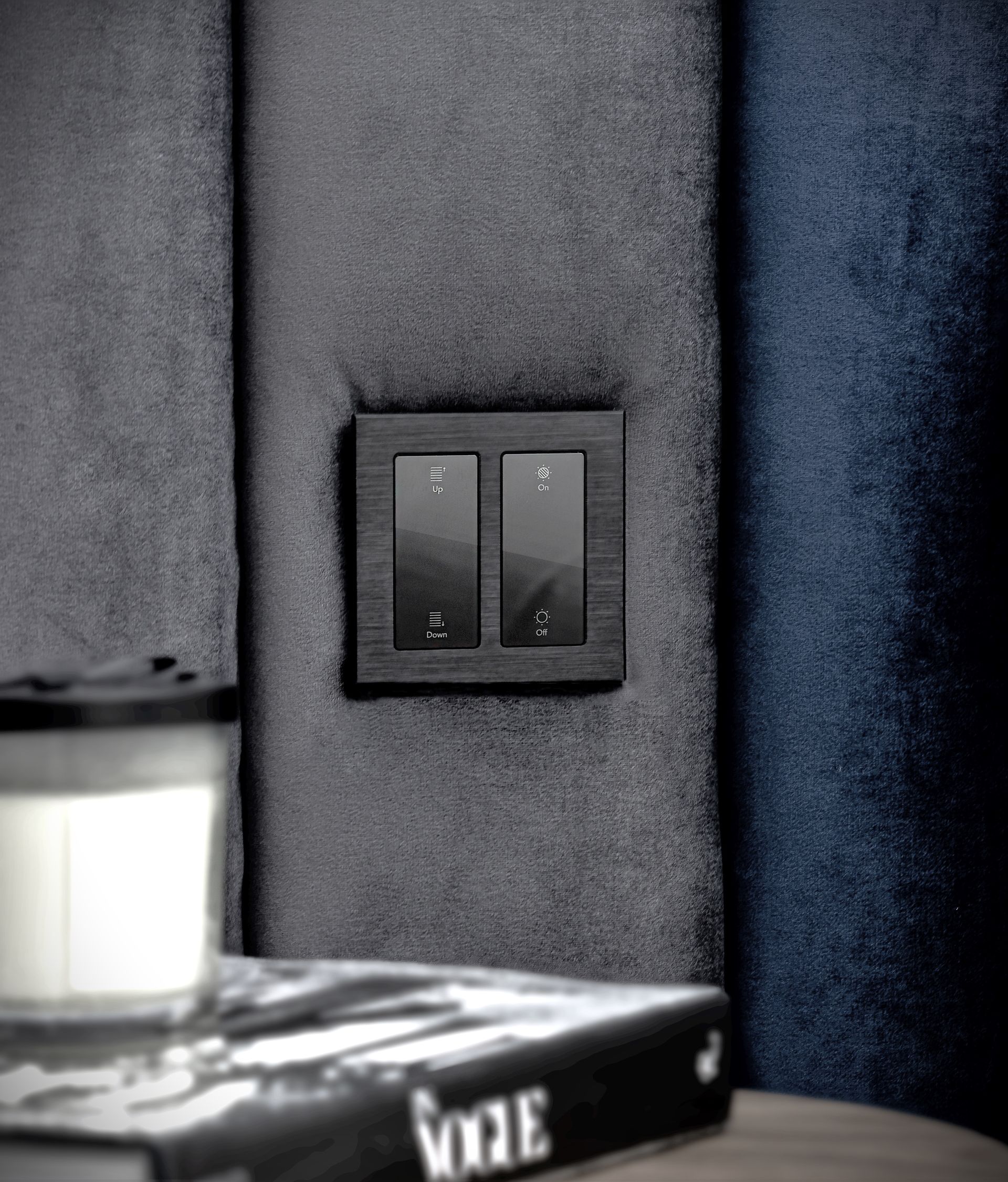 A black light switch is mounted on a wall next to a book and a candle.