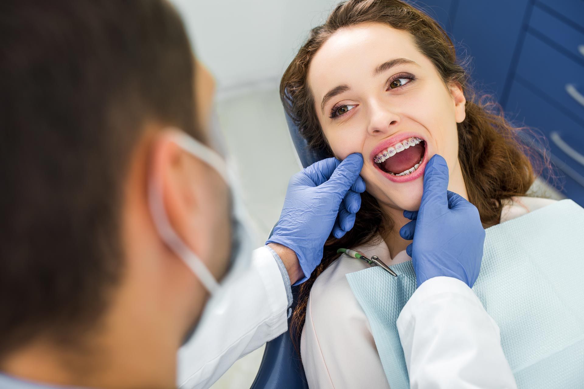 A woman in braces is opening her mouth during an examination of her teeth near a dentist